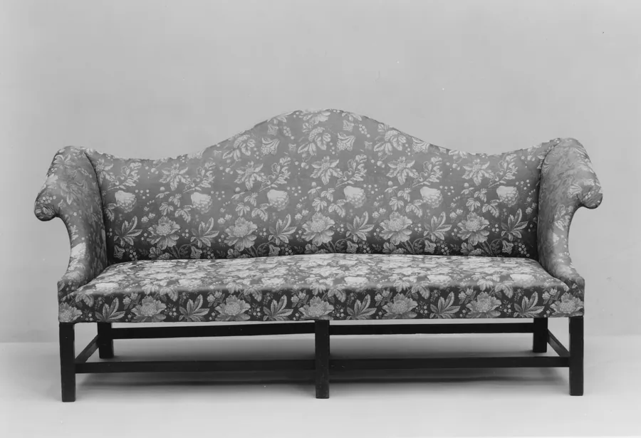 A camelback sofa with floral upholstery, a humped back, scrolled arms and square legs with stretchers