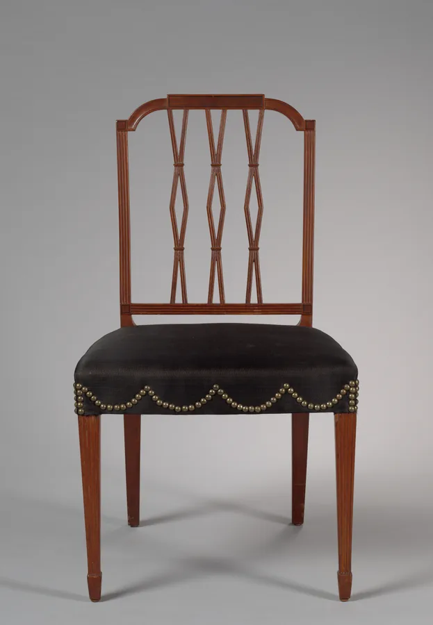 A mahogany dining chair with a square back of three diamond splats, a black upholstered seat and tapered legs