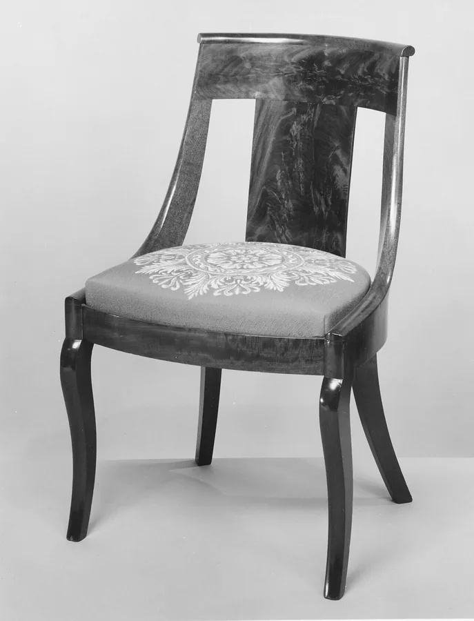 A dark mahogany side chair with a curved gondola back and sabre legs