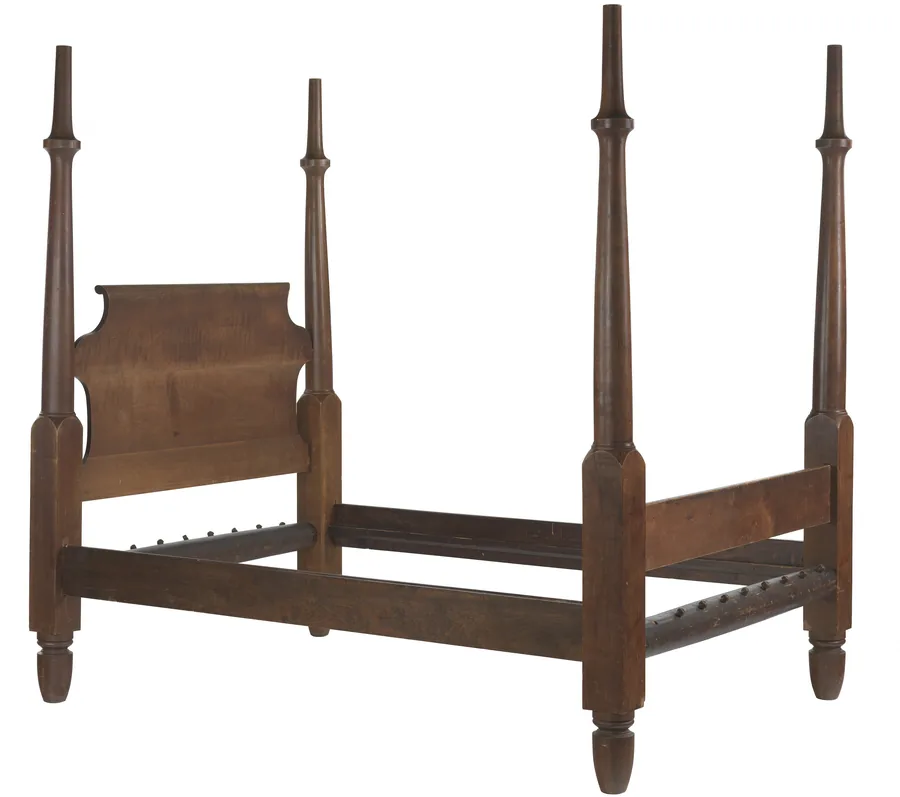A wooden four-poster bed frame with tall tapered posts, a scroll headboard and side rails