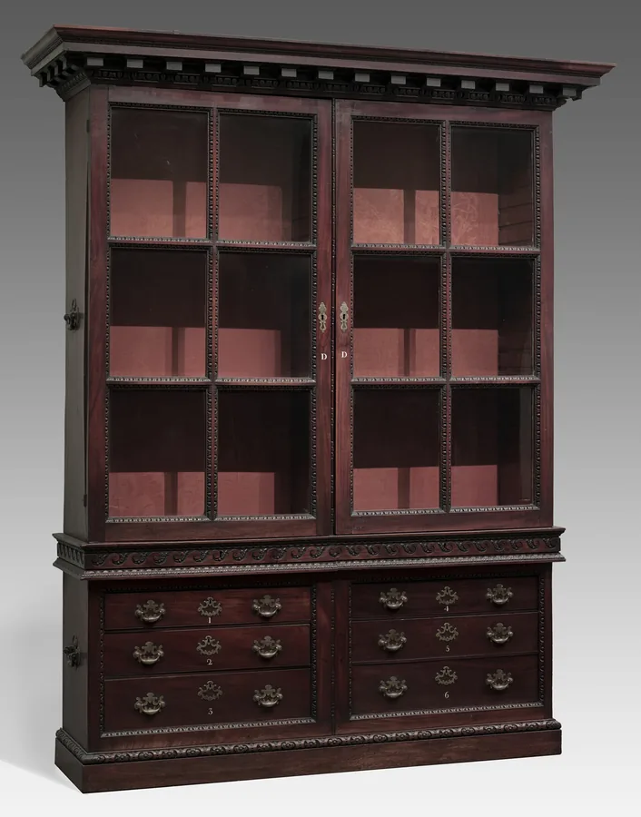 A tall mahogany bookcase with two glazed doors over a base of drawers, under a dentil cornice