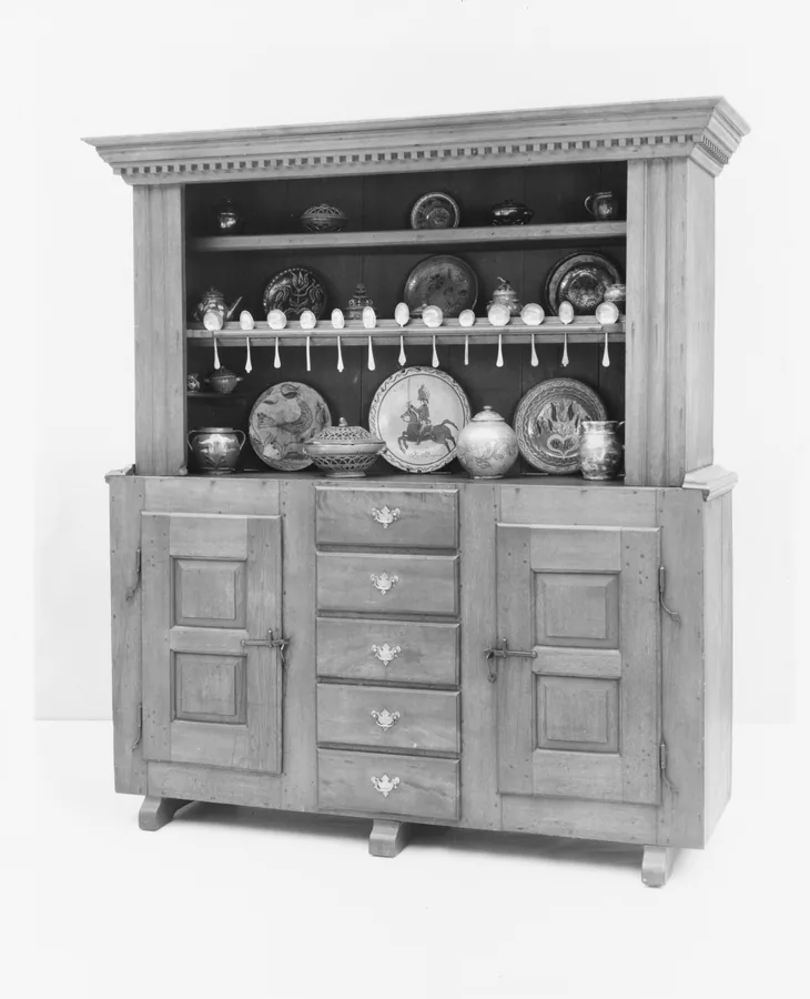 A wooden kitchen dresser with plates on open shelves above, two panelled doors and a column of drawers below