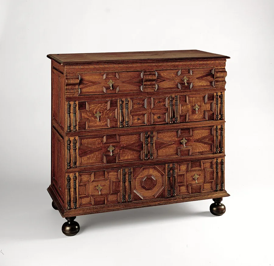 An oak chest of drawers with geometric panels on each drawer and turned ball feet