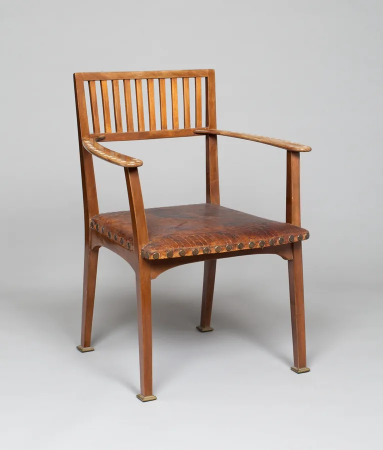 A walnut armchair with a slatted back, flat arms, straight legs and a studded leather seat