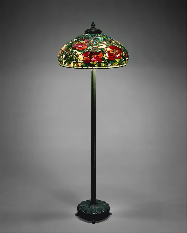 A floor lamp with a domed leaded-glass shade of peonies on a bronze stand
