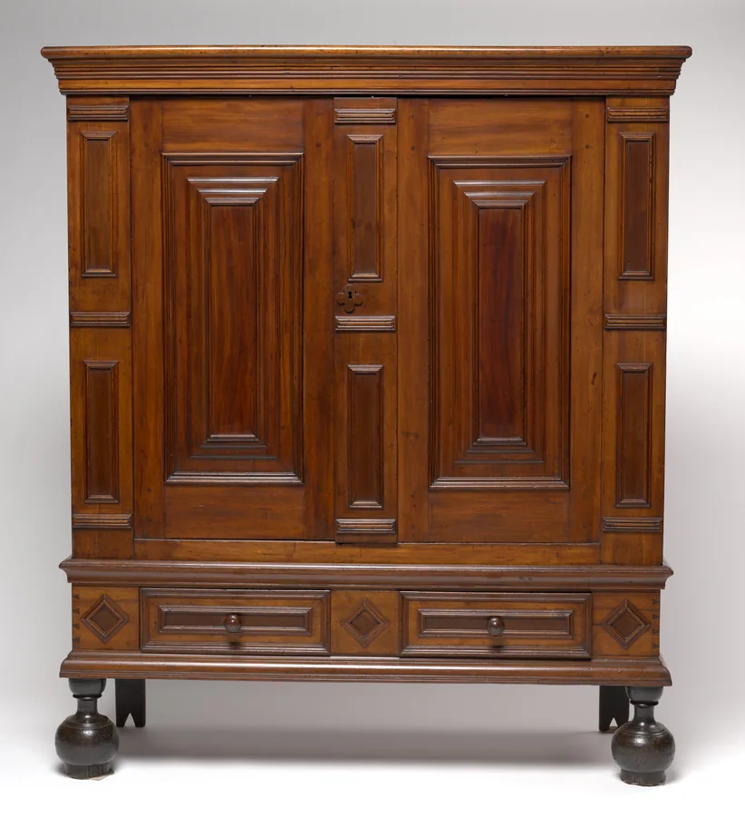 A walnut two-door wardrobe with raised panels, a cornice, a two-drawer base and ball feet